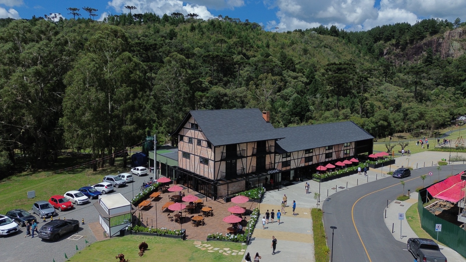 Foto mostra uma imagem aérea do Parque Paraíso das Araucárias. No centro da imagem tem um casarão bege em estilo enxaimel. Ao redor, áreas gramadas e morros verdes atrás.